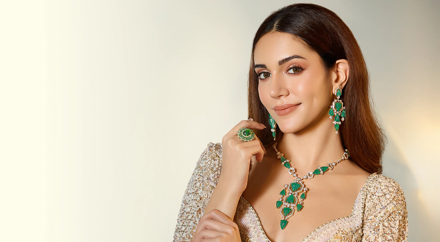 Woman wearing emerald jewelry against a neutral background