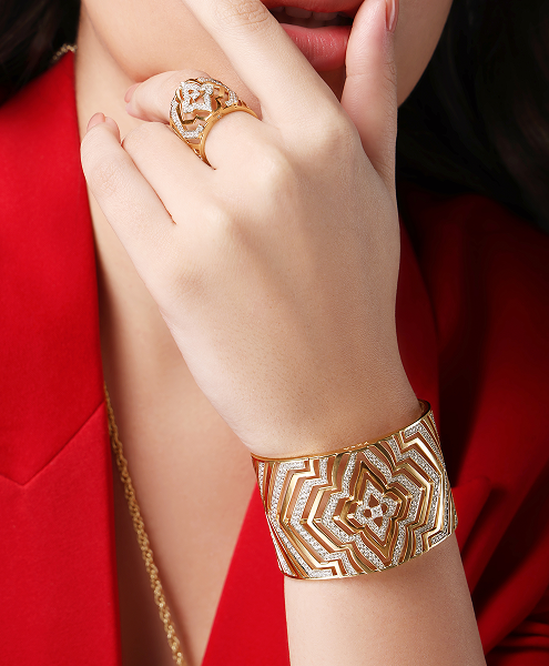 Close-up of a hand wearing a gold ring and bracelet against a red background